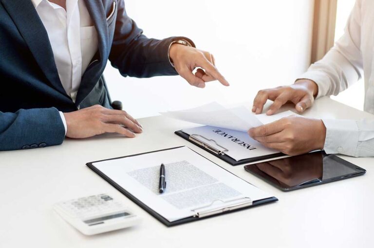 Person reviewing an insurance declaration page beside a calculator, house keys, and organized policy documents.